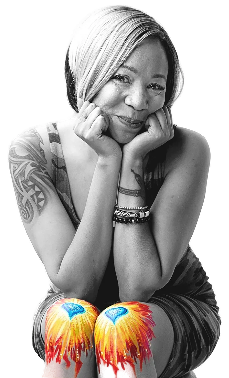 A smiling woman, chin on her hands, with flaming hearts painted on her knees