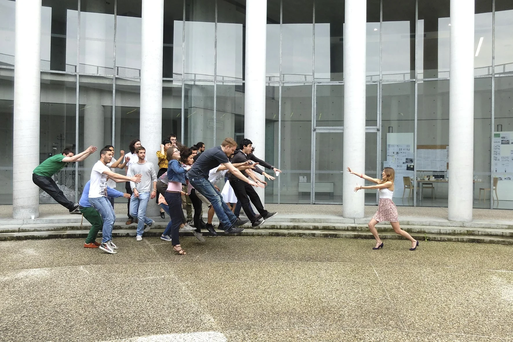 Fabrica researchers leaping toward a woman in front of a glass building