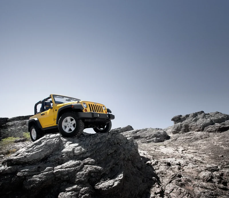 A yellow Jeep Wrangler on a rock outcrop