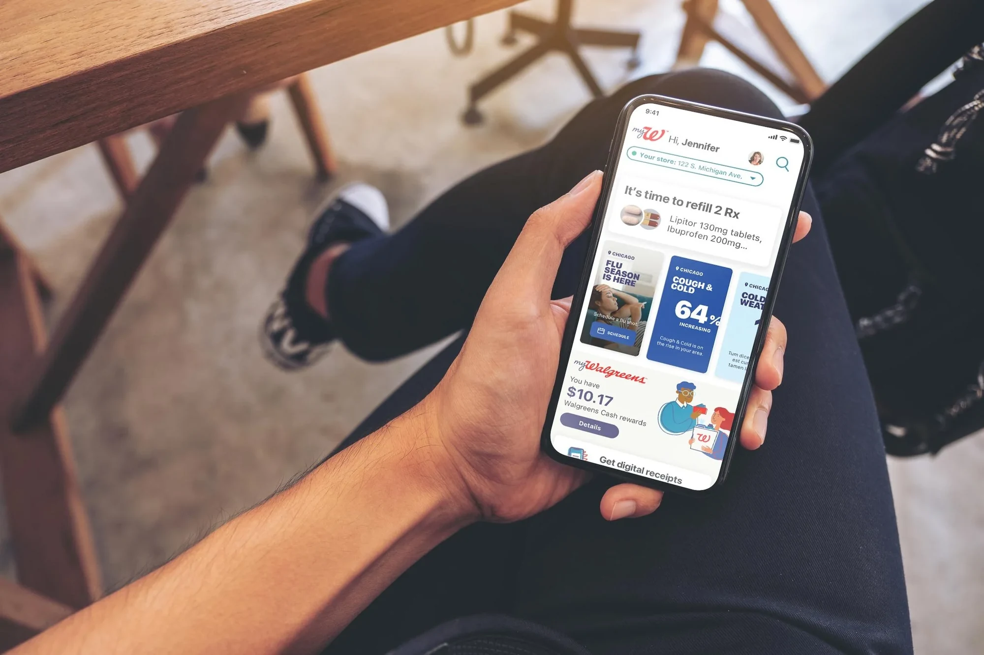 A hand holding a phone showing the MyWalgreens app with a refill reminder and health alerts
